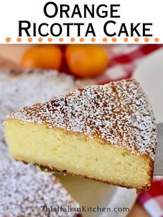 a slice of orange ricotta cake with powdered sugar on top and an orange in the background