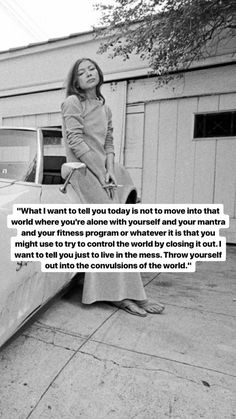 a woman sitting on the hood of a car in front of a building with a quote