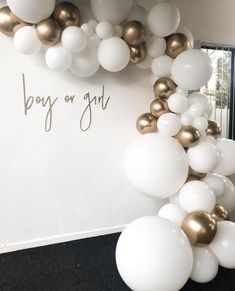 white and gold balloons are hanging from the wall in front of a sign that says boy or girl