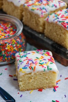 a piece of cake with white frosting and sprinkles next to a jar of sugar