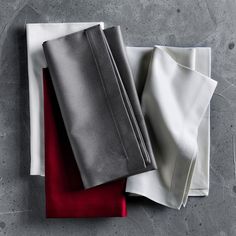 three folded sheets on top of each other with red and white linens next to them