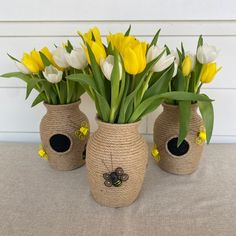 three vases filled with yellow and white flowers on top of a cloth covered table