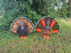 two wooden turkeys sitting on top of a grass covered field next to trees and bushes