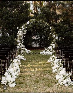 an outdoor ceremony set up with white flowers and greenery on the side of the aisle