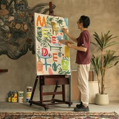 a woman is painting on an easel in front of a wall with art work