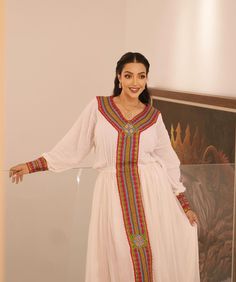 a woman standing in front of a painting wearing a white dress with colorful trims