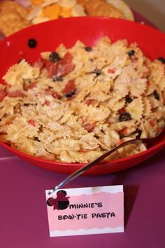 a red bowl filled with pasta next to a sign that says minnie's bowtie pasta