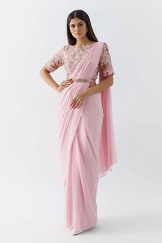 Pink pre-draped saree with pleated cascading hem. Paired with an intricately hand crafted blouse with an attached belt in the front, back cut-out and pleated sleeves hem.
Component: 2
Pattern: Printed, Embroidered
Type Of Work: Floral Motif
Neckline: Boat
Sleeve Type: Half
Fabric: Georgette Crepe, Lining: Shantoon
Color: Pink
Other Details: 
Padded blouse
Cutdana and bead work
Back cut-out blouse
Attached belt
Saree pre draped with draw string and zipper closing
Fully shantoon lining
Closure: Bl Draped Sarees, Drape Saree, Ready To Wear Saree, Half Sleeve Blouse, Pleated Sleeves, Saree Trends, Party Wear Indian Dresses, Indian Fashion Designers, Pink Saree