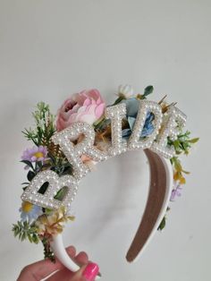 a person holding up a flower crown with the word bride spelled out