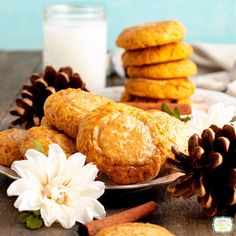 some cookies are on a plate with flowers and pine cones next to it, along with a glass of milk