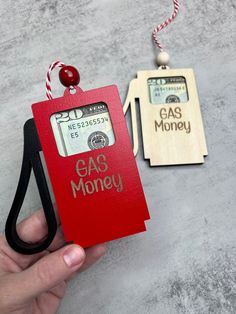 a hand holding a red card with the words gas money attached to it and an ornament that says gas money