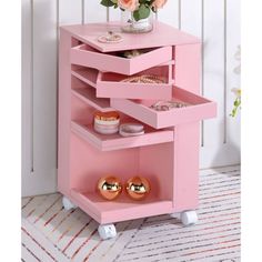 a pink cart with three drawers and gold knobs on the bottom shelf, in front of a white wall