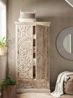 a wooden cabinet sitting in the corner of a room next to a mirror and potted plant