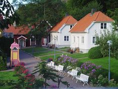 several white benches sitting in the middle of a garden with flowers and trees around them