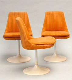 two orange chairs sitting on top of white pedestals