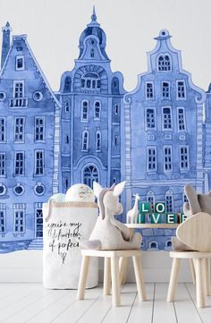 two wooden rabbits sitting on stools in front of a wall with blue buildings behind them