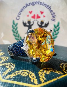 a yellow diamond ring sitting on top of a blue and gold book with an emblem in the background