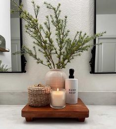 two candles are sitting on a wooden tray in front of a mirror and some plants