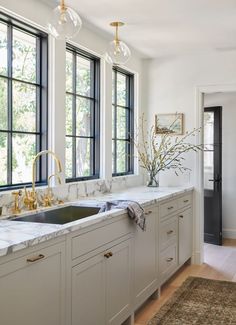 a kitchen with marble counter tops and gold faucets in front of three windows