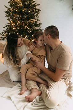 a man, woman and child sitting in front of a christmas tree