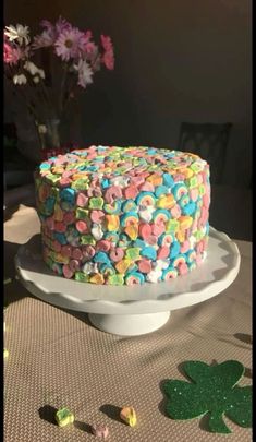 a colorful cake sitting on top of a white plate next to a vase with flowers