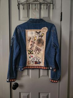 a denim jacket hanging on a door with an embroidered back and side panels that have images of animals