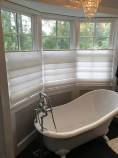 a white bath tub sitting under a window next to a chandelier in a bathroom