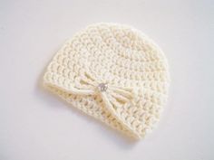 a white crocheted hat with a bow on the side and a diamond in the middle