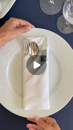 two hands holding silverware over a white plate with wine glasses and napkins on it