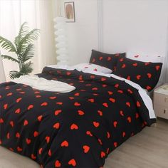 a bed with black and red hearts on it in a room next to a potted plant