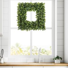 a kitchen window with a boxwood wreath hanging over the sink in front of it