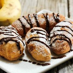 several pastries on a white plate with chocolate drizzled on them and bananas in the background