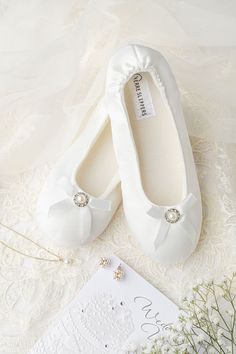 two pairs of white shoes with bows on them next to a wedding card and flowers