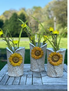 three vases with sunflowers in them sitting on a wooden table outside,