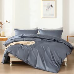 a bed with blue sheets and pillows in a white room next to a wooden floor