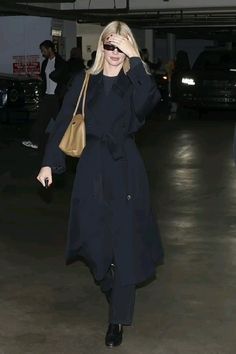 a woman walking through an airport carrying a brown purse and wearing black clothing with her hand on her head