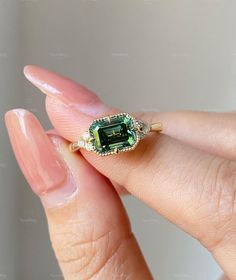 a woman's hand holding an emerald and diamond ring