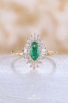 an oval shaped emerald and diamond ring on a white surface with a gold band around it