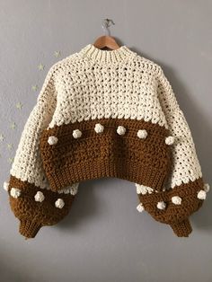 a knitted sweater hanging up on a wall next to a wooden hanger with white and brown crochet