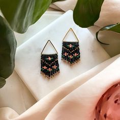 two pairs of beaded earrings sitting on top of a white cloth next to a potted plant