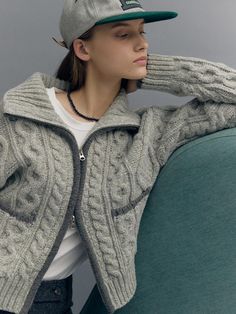 a woman wearing a baseball cap and sweater is sitting on a couch with her hands behind her head