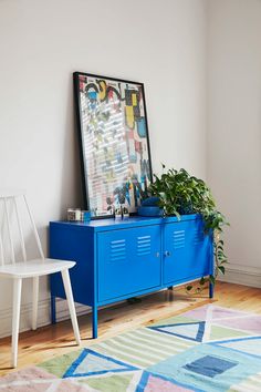 a blue cabinet with a plant on top and a white chair in the corner next to it