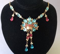 "Old gold tone, vibrant jewel tone rhinestone necklace.  Bohemian designs were very colorful and varied. Some pendants had more, others, less, glass stones.  This beautiful Czech or Austrian from the 1920's has more gems and they are placed in attractive patterns of deep pink, blue and clear.  Some are prong set and others are bezel set.   Gorgeous!  Minor wear after 100 years.  Some of the foiled backing is peeling. (Photo # 8) The blemishes don't seem to interfere with the beauty of the piece.  There is some staining on the brass back plate, also.  Please enlarge and look carefully.  All gems are intact.  Nice gilt brass wheat chain.  Unusual craftsmanship.  The extra loops are apparently not for additional gems.  Dimensional.  About 3/4\" high.  Necklace is 17 1/2\" long  Pendant: 1 7/8 Rhinestone Pendant Necklace, Costume Jewelry Style, Vintage Rhinestone Pendant Jewelry, Jeweled Costume Jewelry Necklaces For Evening, Vintage Gold Multi-stone Necklace, Costume Jewelry Rhinestone Pendant Necklace, Vintage Pendant Necklace With Rhinestones, Vintage Rhinestone Pendant Necklace, Antique Jeweled Necklaces For Party, Costume Jewelry Rhinestone Necklace