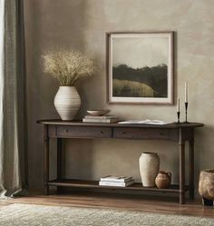 a wooden table with two vases and a painting on the wall above it in a room