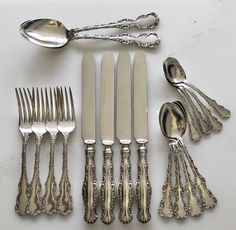 an assortment of silverware including forks, knives and spoons on a white surface