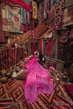 a man and woman standing in front of rugs on the ground with their backs to each other