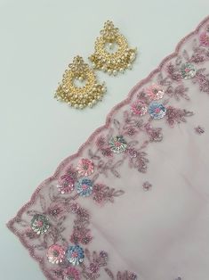 two pairs of earrings are sitting on a table next to a pink cloth with sequins