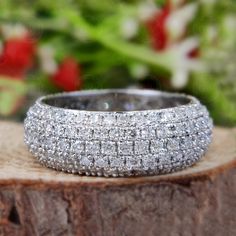 a diamond ring sitting on top of a piece of wood with flowers in the background