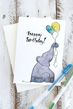 an elephant holding balloons with the words happy birthday written on it's side and two pens next to it