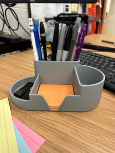 an office desk with pens, markers and sticky notes in a holder next to a keyboard